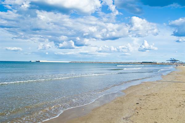 Golden sand and gentle waves, industrial port on the horizon under white clouds