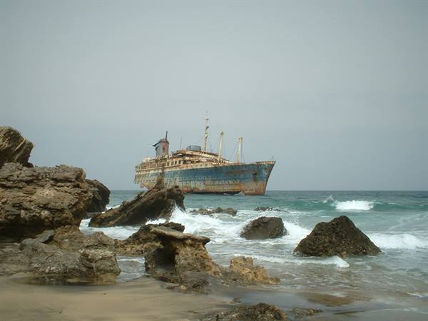 Rusty shipwreck stranded on rocks, waves crashing under grey sky