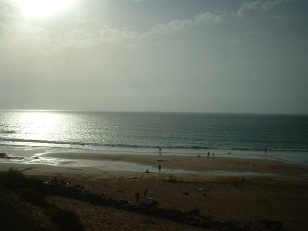 Hazy sun over dark sandy beach with people in the waves