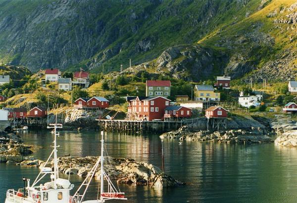 Red wooden houses on the water beneath green mountains, fishing boat in foreground