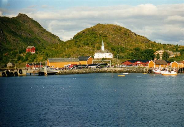 Boats in the harbour, red and yellow wooden houses, white church beneath green hills