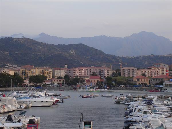 Boats moored in the harbor before pastel buildings and misty mountains