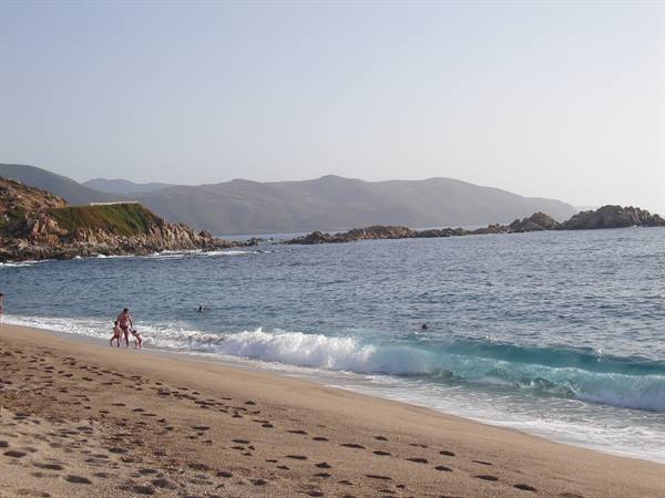 Children playing in the surf on a sandy beach with rocks and hills behind
