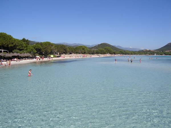 Swimmers wading in shallow turquoise water near a sandy beach with umbrellas