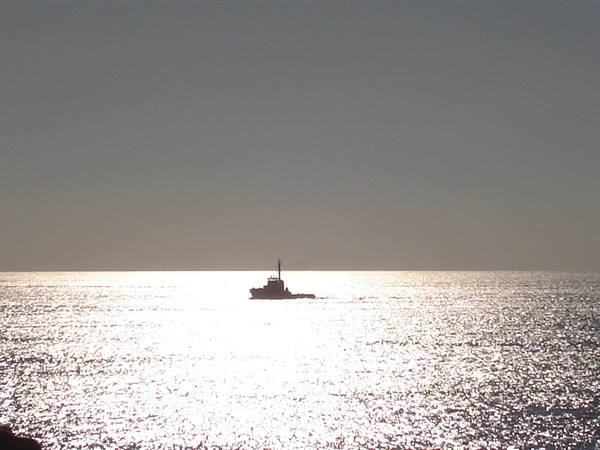 Silhouetted ship on sparkling sea, silver reflections on the water