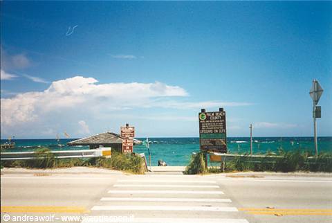 Crosswalk leading to the beach, green sign, turquoise sea under white clouds