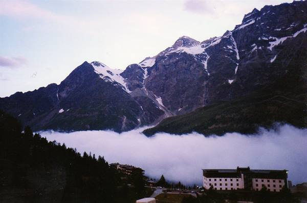 Low clouds blanket the valley beneath snow-capped peaks, building in foreground