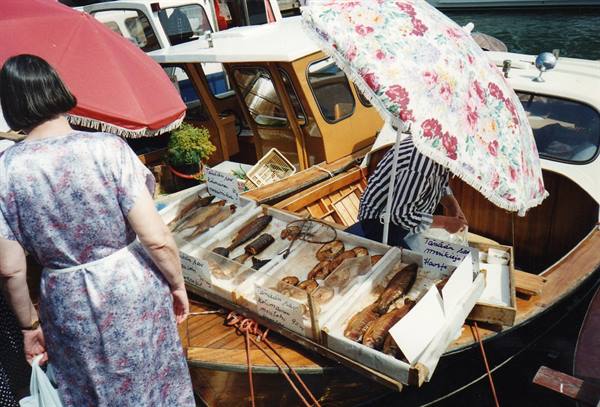 Woman sells fresh fish from a wooden boat under floral umbrella