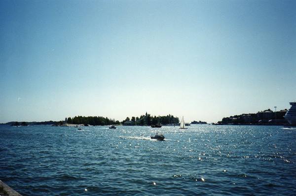 Speedboat and sailboat among islands, sparkling sea under sunny sky