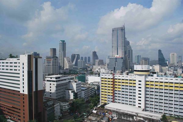 Glass skyscrapers above yellow and white buildings, bright clouds, Bangkok