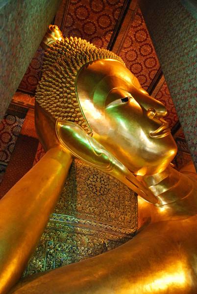 Golden head of the Reclining Buddha at Wat Pho, under decorated ceiling