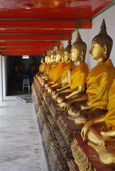 Row of golden Buddha statues draped in yellow cloth beneath a red decorated ceiling