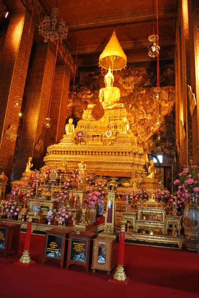 Large golden Buddha under umbrella inside Wat Pho temple, flower offerings