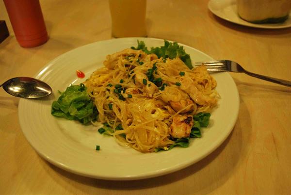 Plate of rice noodles with chicken and lettuce, cutlery on wooden table