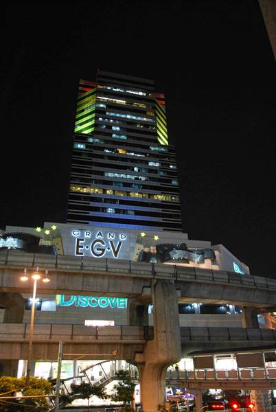 Illuminated skyscraper at night above Grand EGV cinema and elevated train tracks