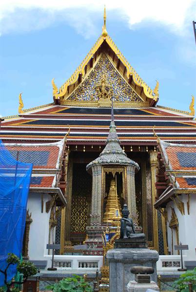 Golden temple with pointed roof, golden stupa and bronze statue before the entrance, Bangkok