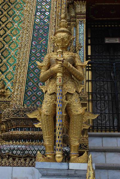 Golden yak guardian statue at Wat Phra Kaew, glass mosaic walls behind