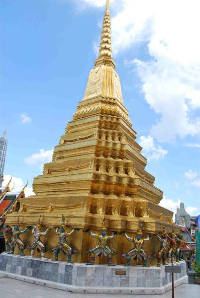 Golden stupa at Wat Phra Kaew, guardian yaksha statues around base, blue sky