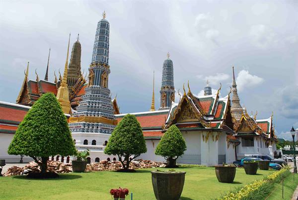 Gleaming prangs and golden roofs of Bangkok's Grand Palace under cloudy sky
