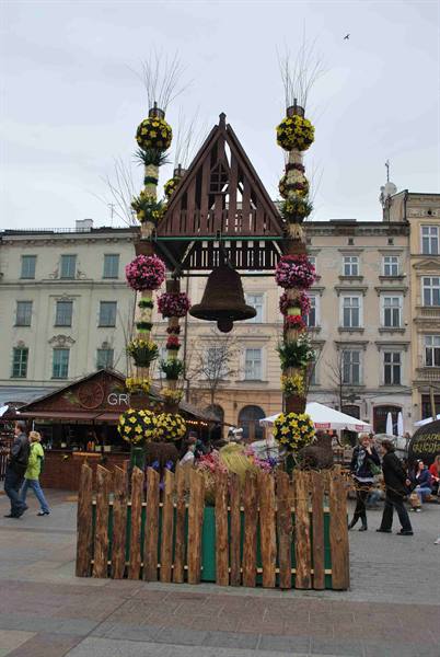 Wooden bell under a small roof, decorated with flower garlands, in the square