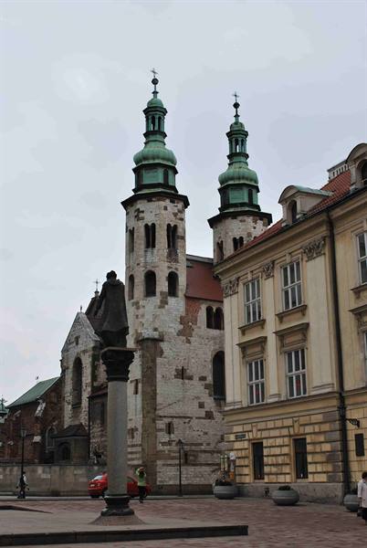 Romanesque church with two green spires, column statue and yellow building, Kraków