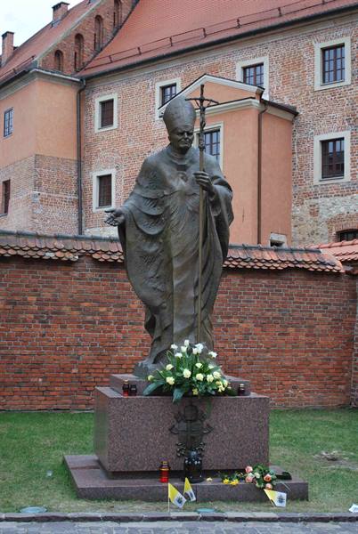 Bronze statue of Pope Wojtyła with flowers, before Frombork's brick castle