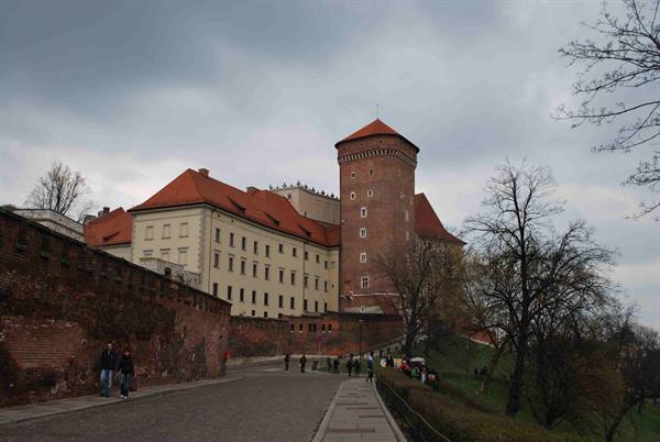 Tourists walk beneath brick walls and the red tower of Wawel Castle