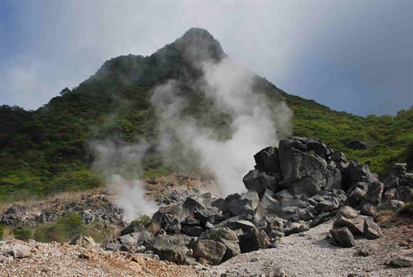 Geothermal steam rising among black rocks and green mountain, Owakudani