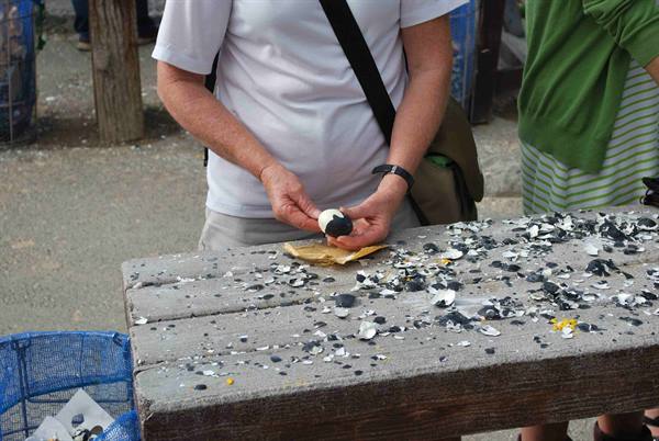 Tourist peeling a hard-boiled egg at a wooden table covered with shells