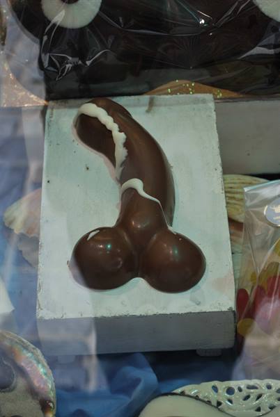 Chocolate phallic-shaped pastry displayed in a shop window on white tray
