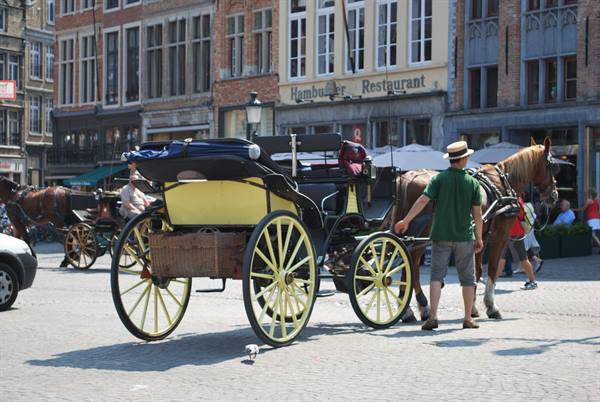 Horse-drawn carriage with yellow wheels on cobbled square beside medieval guildhalls
