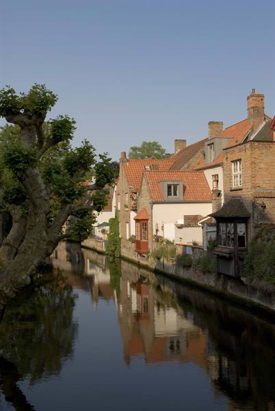 Brick-roofed houses reflect in a calm canal in Bruges