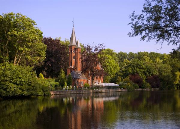 Red brick castle with tower among trees reflected in Bruges lake