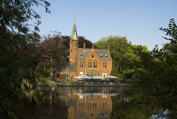 Red brick castle with spire reflected in Minnewater lake, Bruges