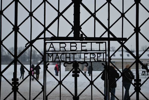 Iron gate with Arbeit Macht Frei sign, visitors in snow at Dachau