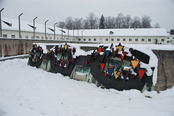 Dachau memorial: colored triangles on walls, snow-covered white barracks under grey sky