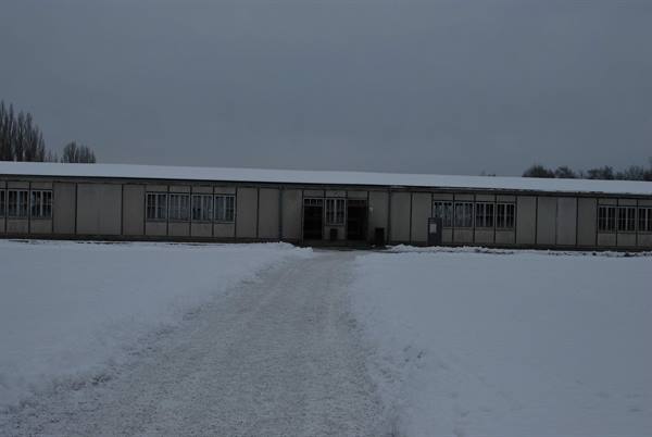 Long wooden barracks covered in snow, trodden path to the entrance, grey sky