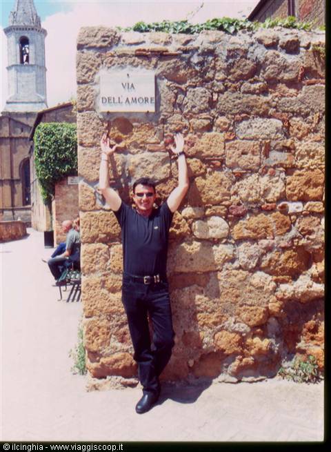 Man leaning on tufa wall under Via dell'Amore sign, bell tower behind
