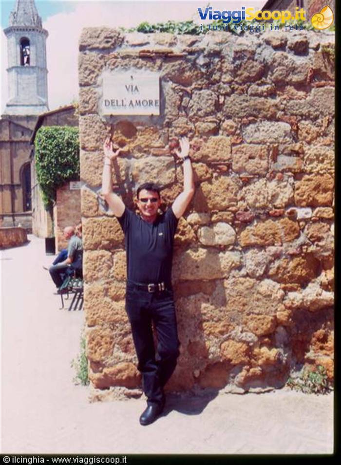 Man leaning on tufa wall under Via dell'Amore sign, bell tower behind