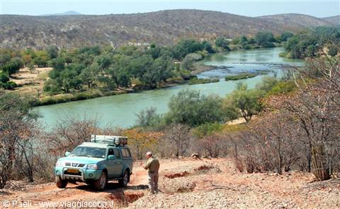 Off-road vehicle on dirt track beside a green river between arid hills