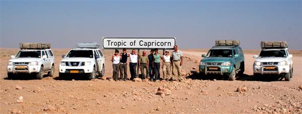 Travelers and 4x4s posing under the Tropic of Capricorn sign in the desert