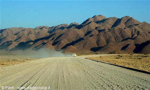 Car raising dust on gravel road among arid brown mountains