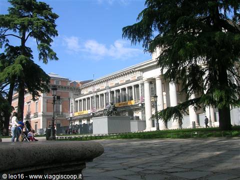 Prado Museum facade framed by trees, person with stroller on the square