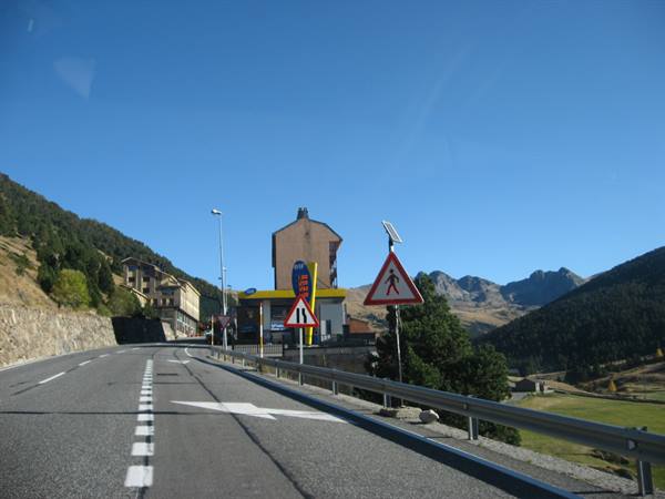 Mountain road with guardrail, traffic signs and a gas station among the peaks