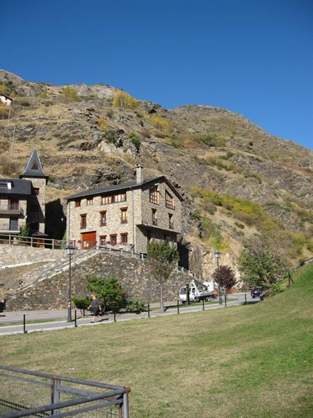 Stone house beneath rocky mountains, green lawn and white truck on road