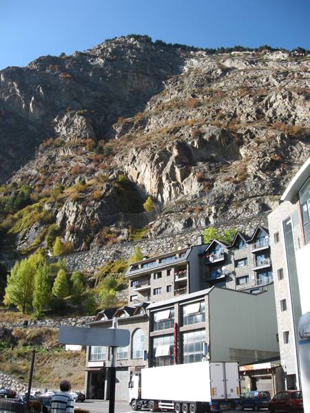 White truck parked beneath stone buildings, rocky mountain towering above Andorra la Vella