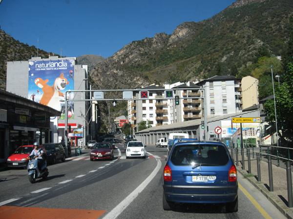Cars and scooter at traffic lights on a road with Naturlandia sign among mountains