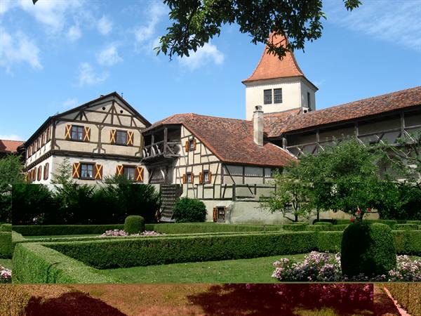 Half-timbered houses with red-tiled tower above a hedge garden