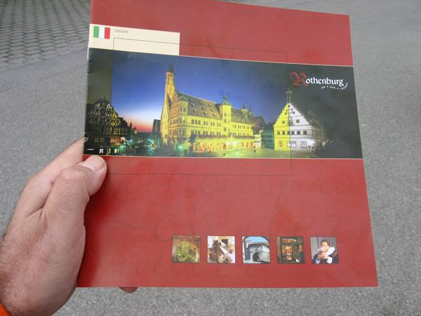 Hand holding a red Rothenburg brochure showing the illuminated town hall