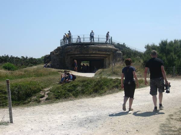 Tourists on the old concrete bunker at Pointe du Hoc, walking along sandy path